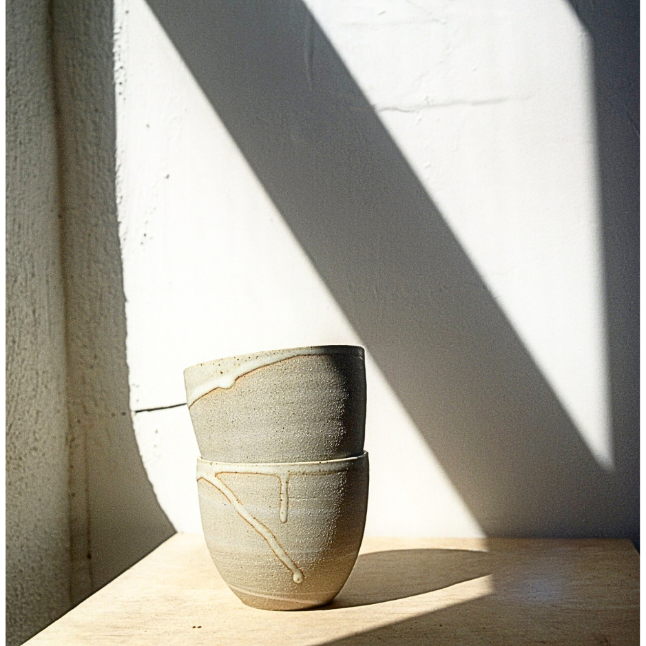 A beige ceramic mug with a white glaze, sitting on a surface with a shadow cast over it.