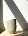 A beige ceramic mug with a white glaze, sitting on a surface with a shadow cast over it.